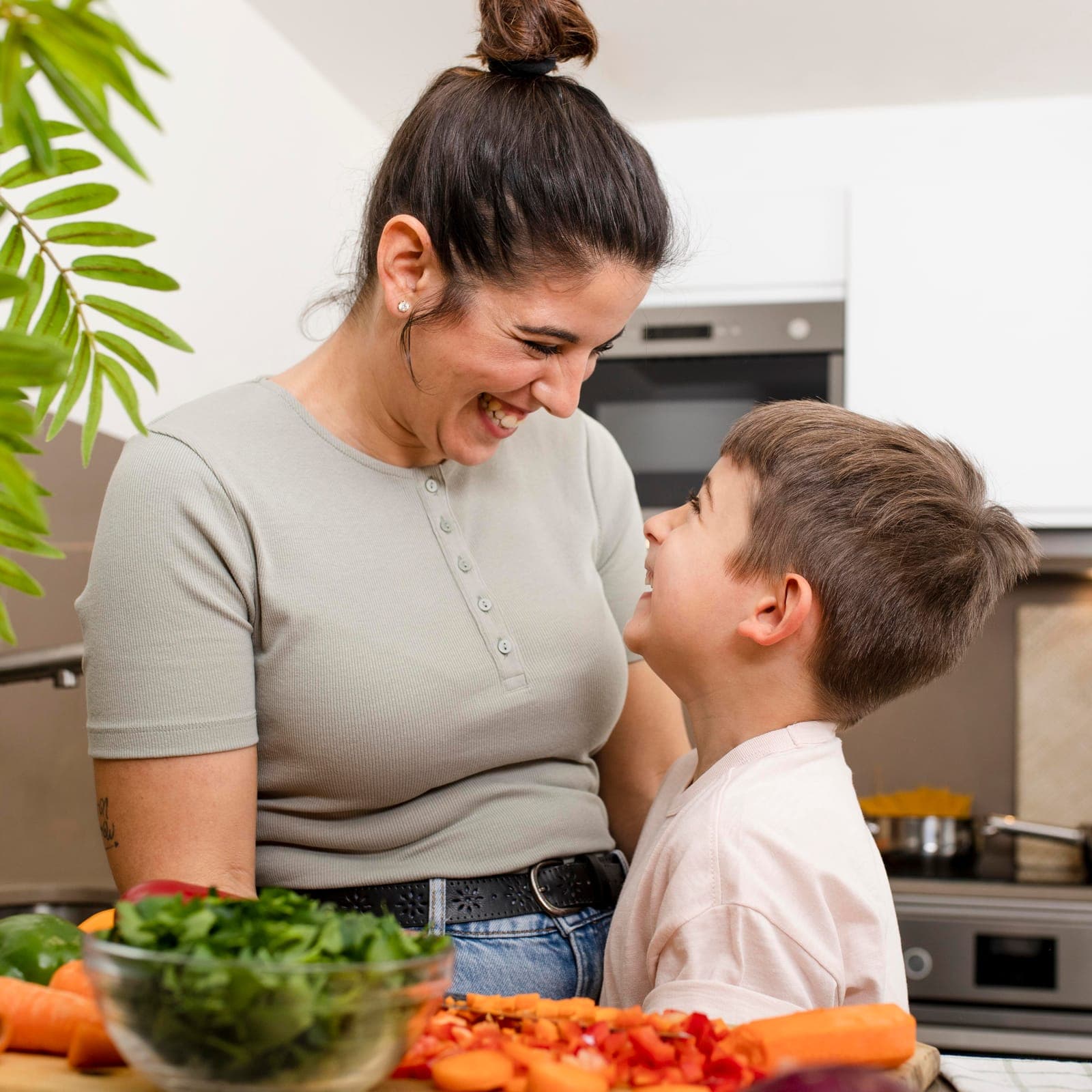 Mãe e filho rindo juntos na cozinha, com legumes já cortados na bancada